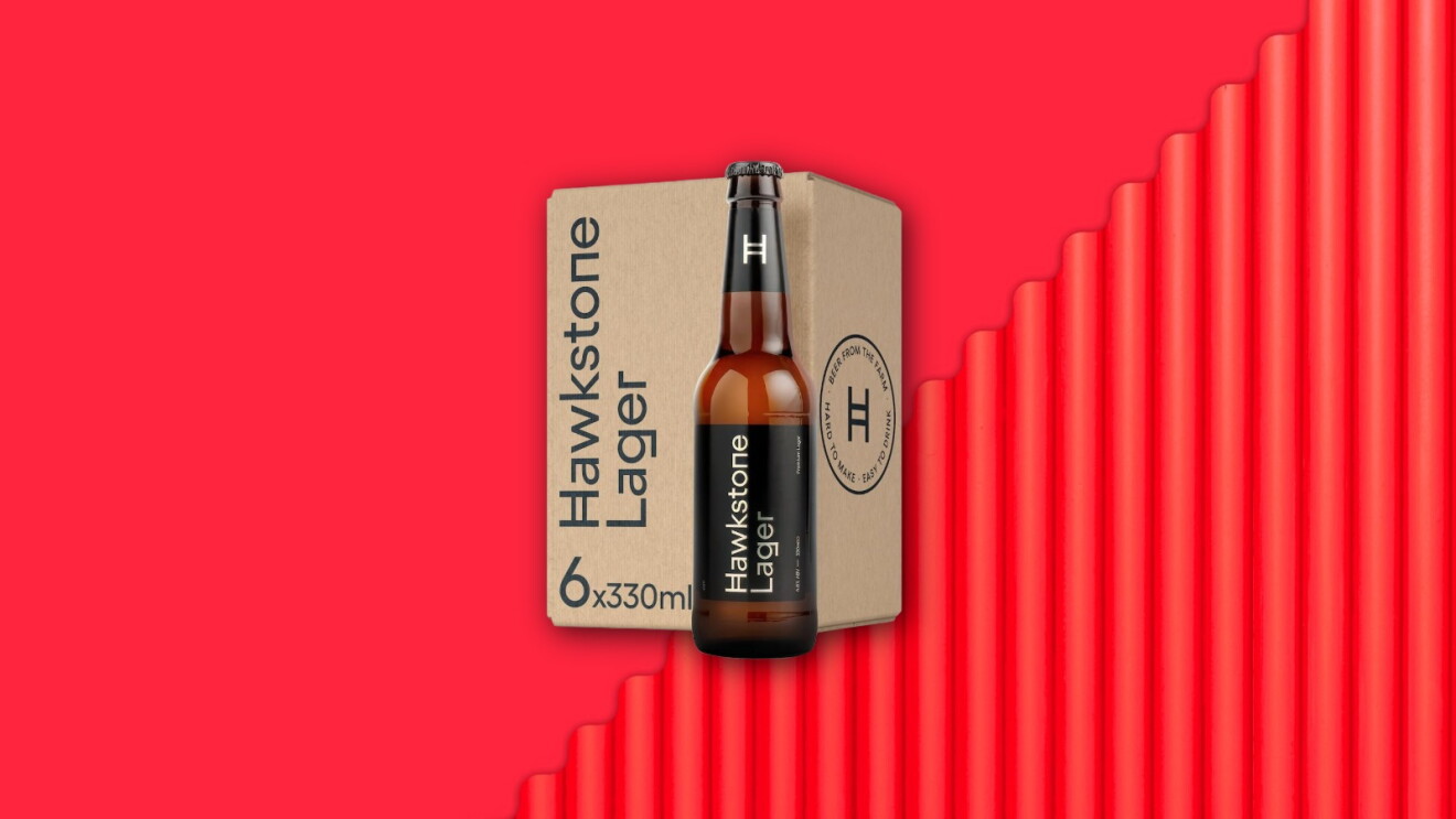 Hawkstone Lager beer bottle next to its six-pack box on vibrant red background
