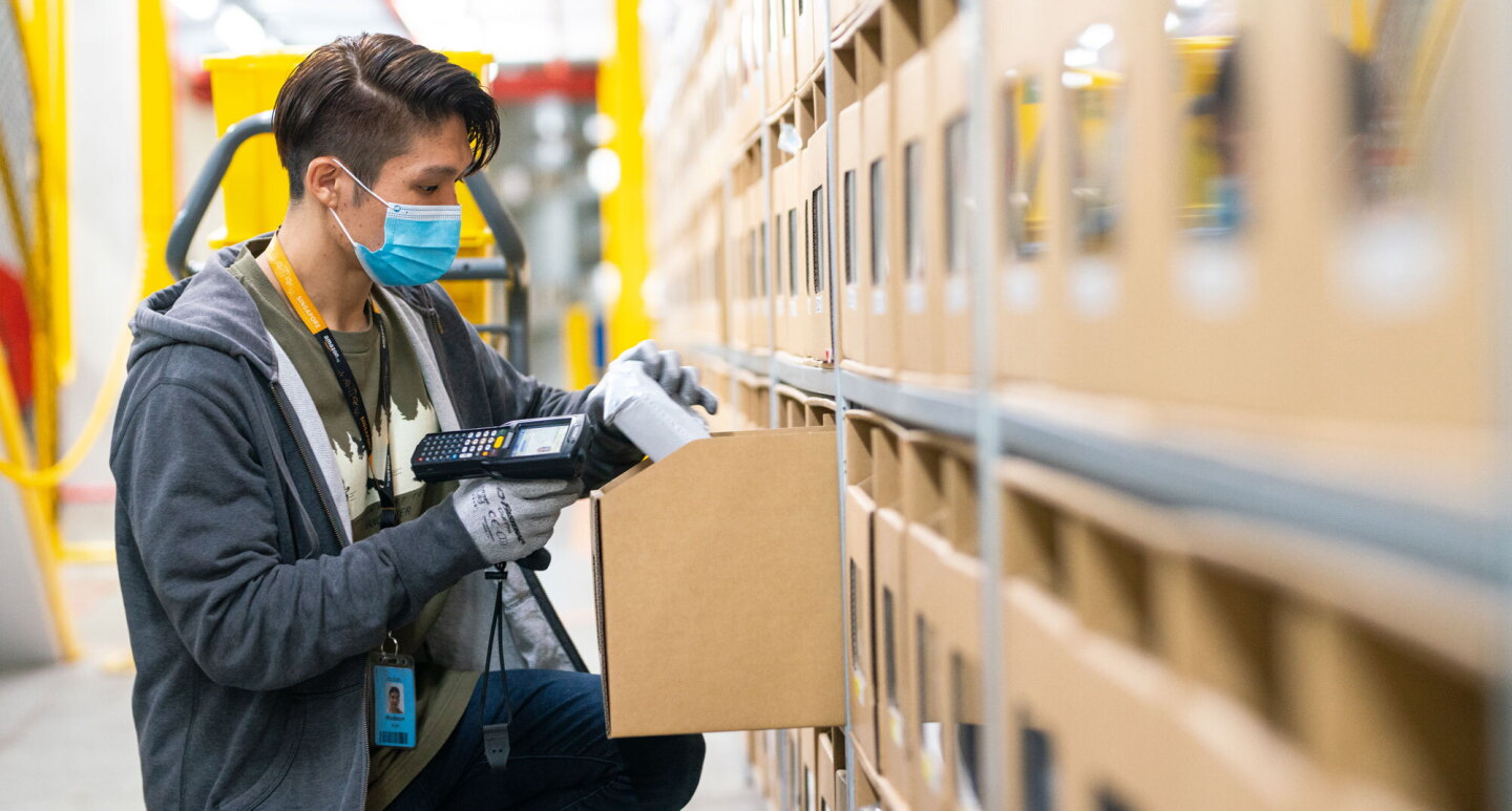 An Amazon employee wearing a face mask scans an item in a fulfilment centre.