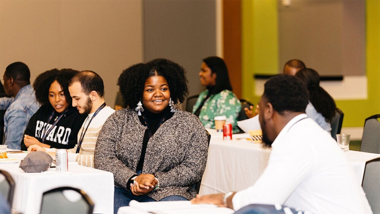 一个女人的形象在一次会议上穿着一件灰色的毛衣和说话人在她旁边。