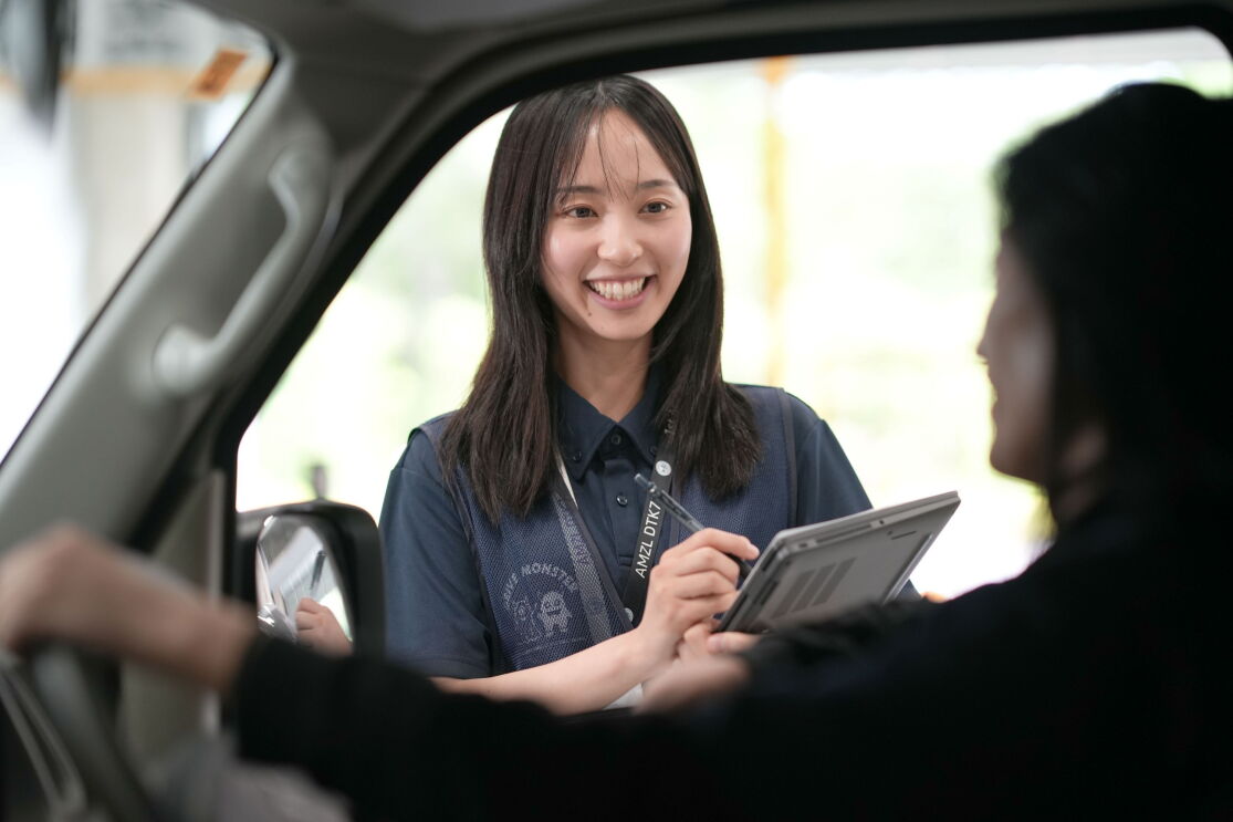 女性が車の外に立ち、メモをとりながら車の運転席に座っている女性と話し合っている