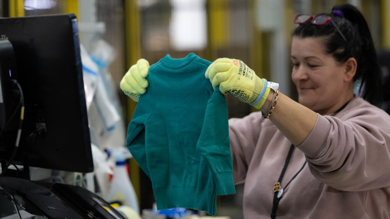 An Amazon fulifillment center employee holding up and inspecting a returned sweater