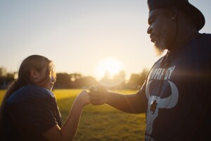 A football coach and a player fist bump. The player is a female little league player.