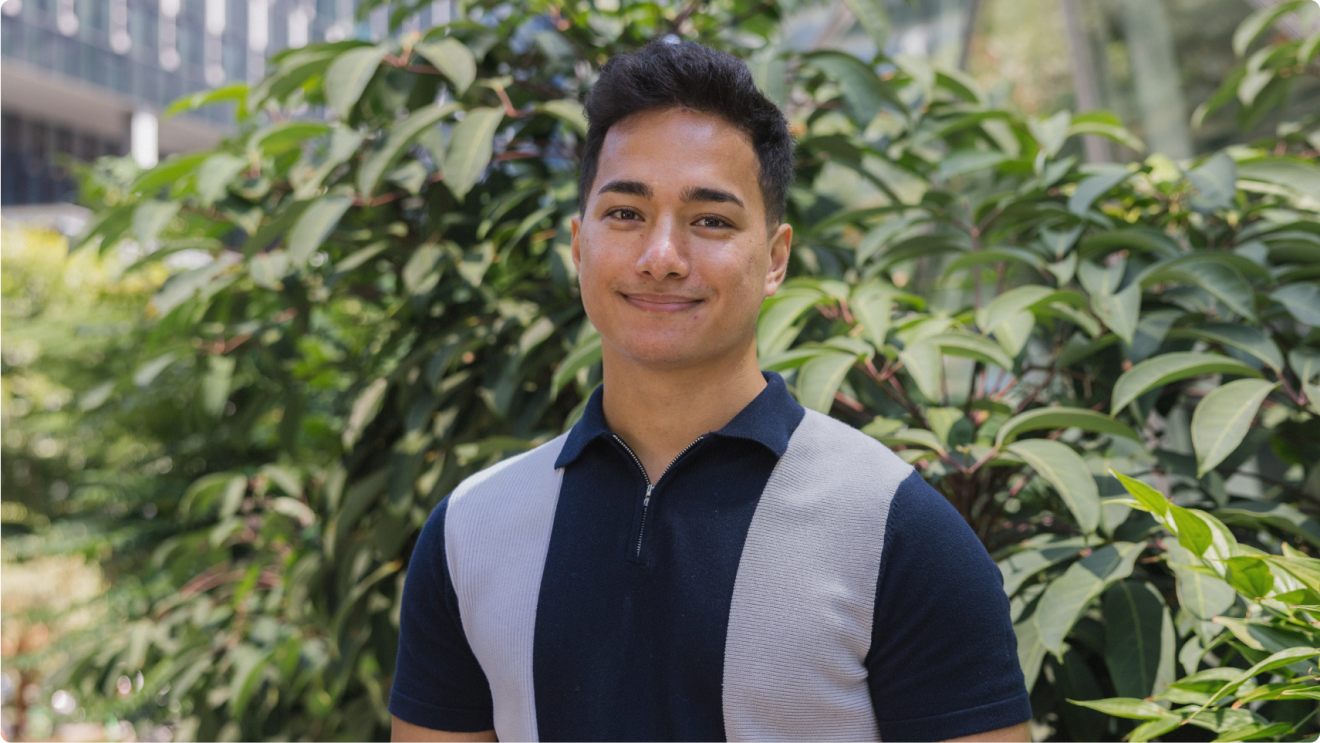 Man smiling to camera in front of foliage