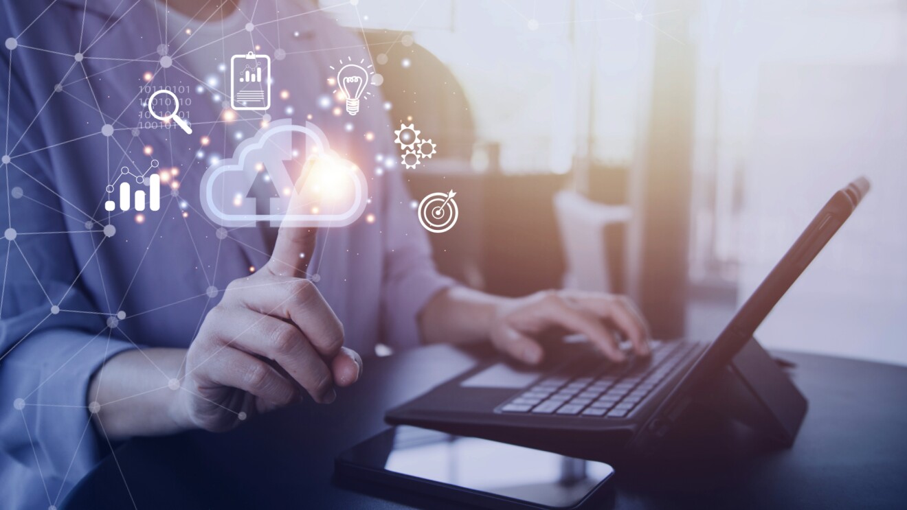 Eine Frau hält einen Laptop in der Hand und tippt mit dem Zeigefinger auf ein virtuelles Cloud-Symbol.