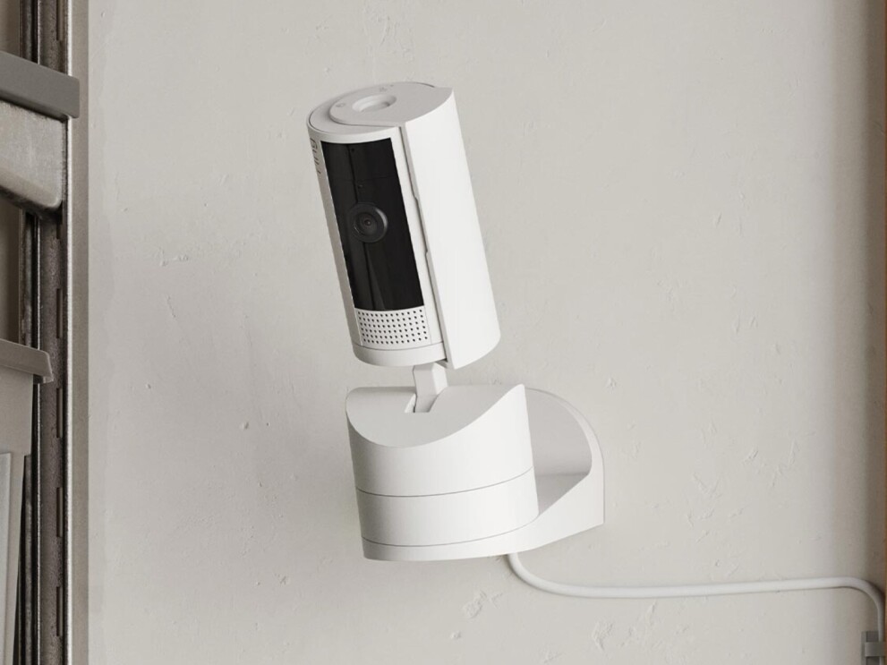 壁に固定されている白い円筒状のセキュリティカメラ Ring(リング)。そのリングの左側にはスチール製の棚がある