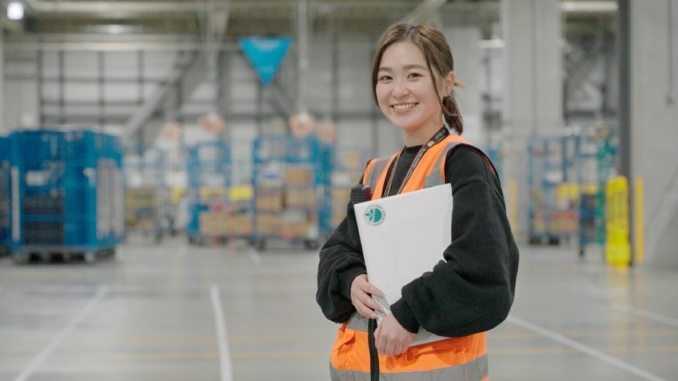 広い作業スペースでオレンジのベストを着た女性ラップトップPCを抱えている