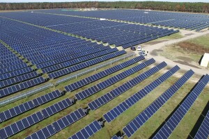 A solar farm with a few cars parked and people looking around.