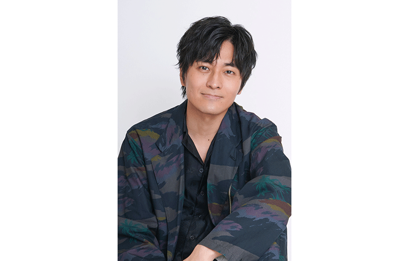 薄いグレーの背景に、彩度の低い迷彩柄のジャケットを着た男性のポートレート。