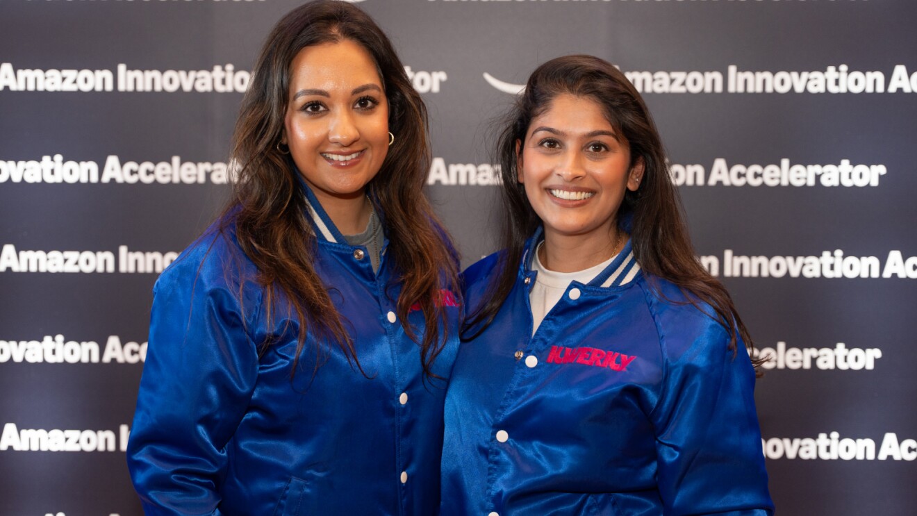 Two women in blue Amazon Innovation Accelerator jackets smiling at event