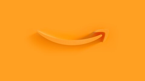 Amazon's orange smile logo appears as an extruded plastic form on an orange background, with a shadow cast by a light source from the right