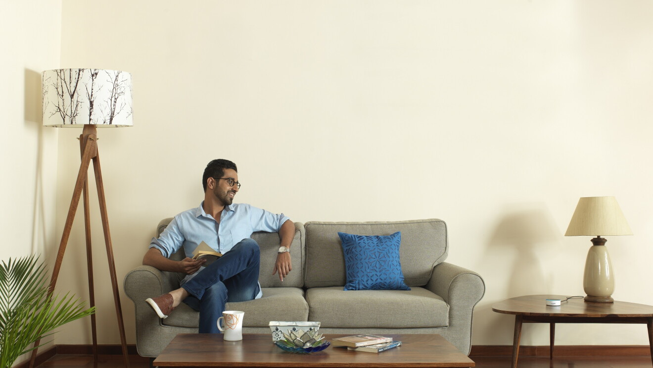 A man sits on a sofa in what looks like he is interacting with Alexa
