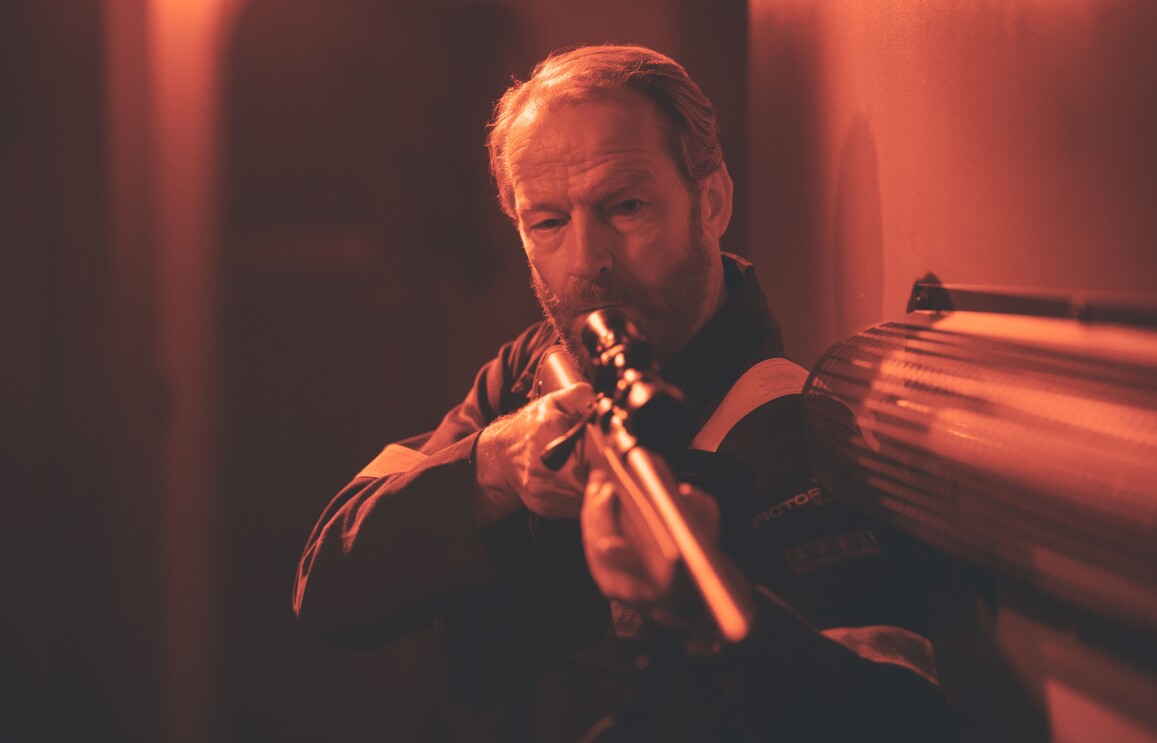 Iain Glen holding a weapon in a dark room in The Rig season 2