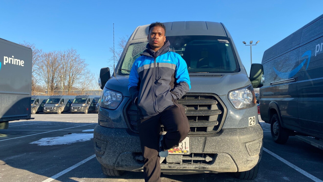 Jaren wears his Amazon jacket and stands in front of one of his Amazon delivery vehicles.