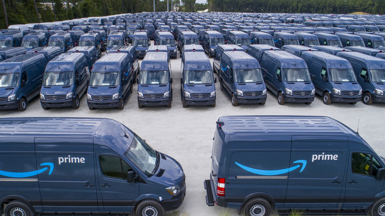 Two navy Mercedes-Benz vehicles with Amazon Prime branding on the side. Behind them, dozens of identical vehicles.