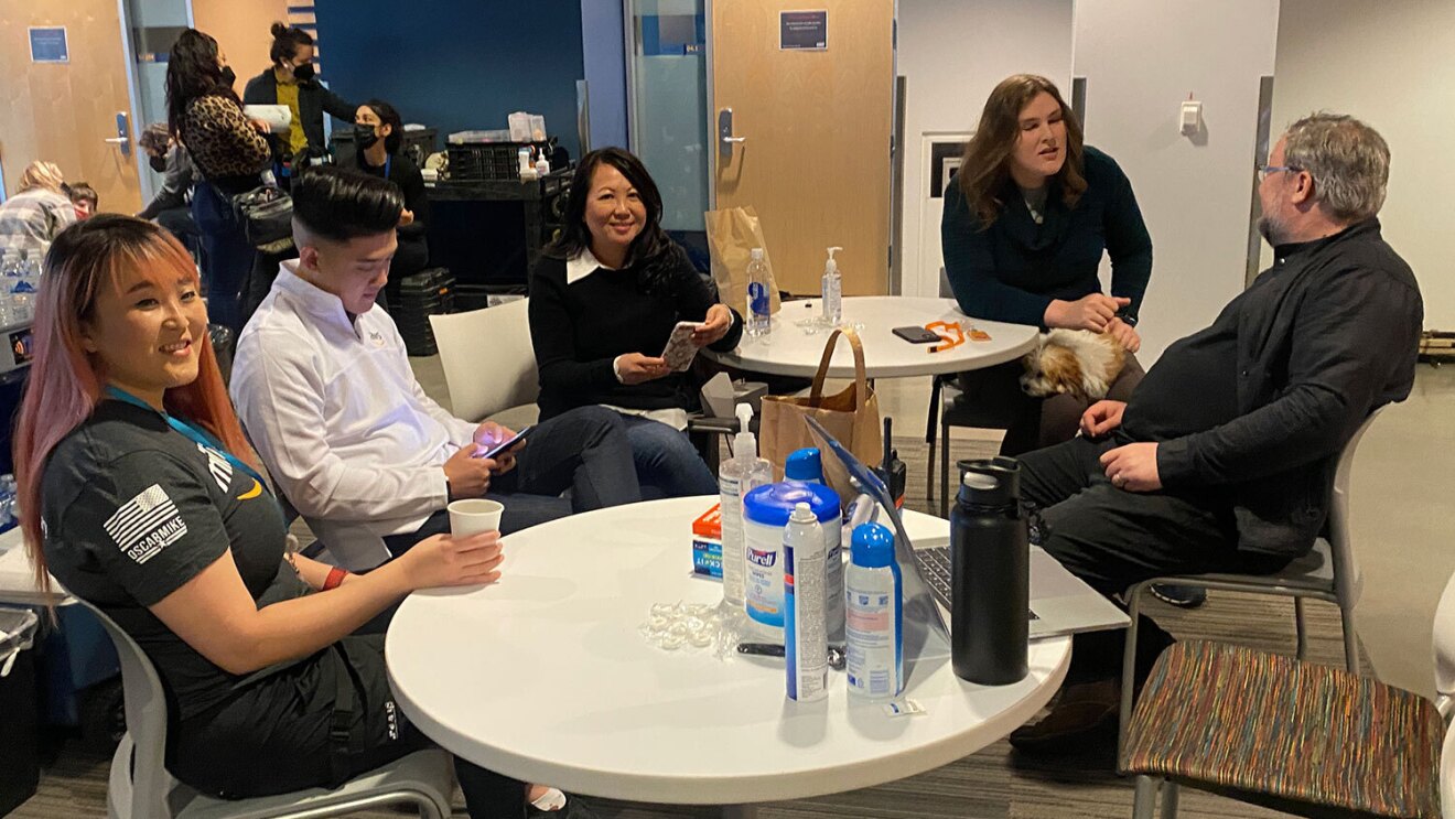 An image of a group of people sitting around a table talking to one another.