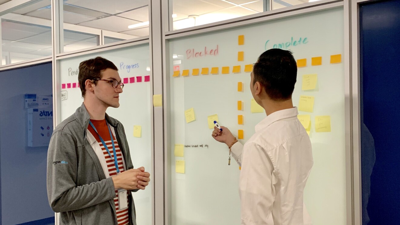 Two men stand together, working on a whiteboard in an Amazon office. 