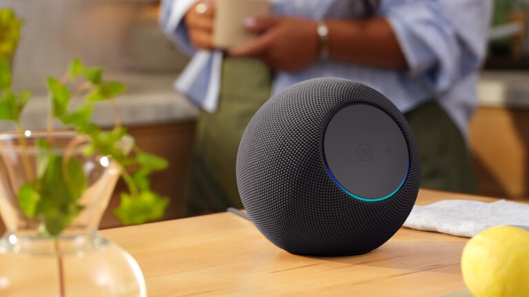 Amazon Echo on a kitchen counter on a sunny day, with a woman drinking tea in the background.