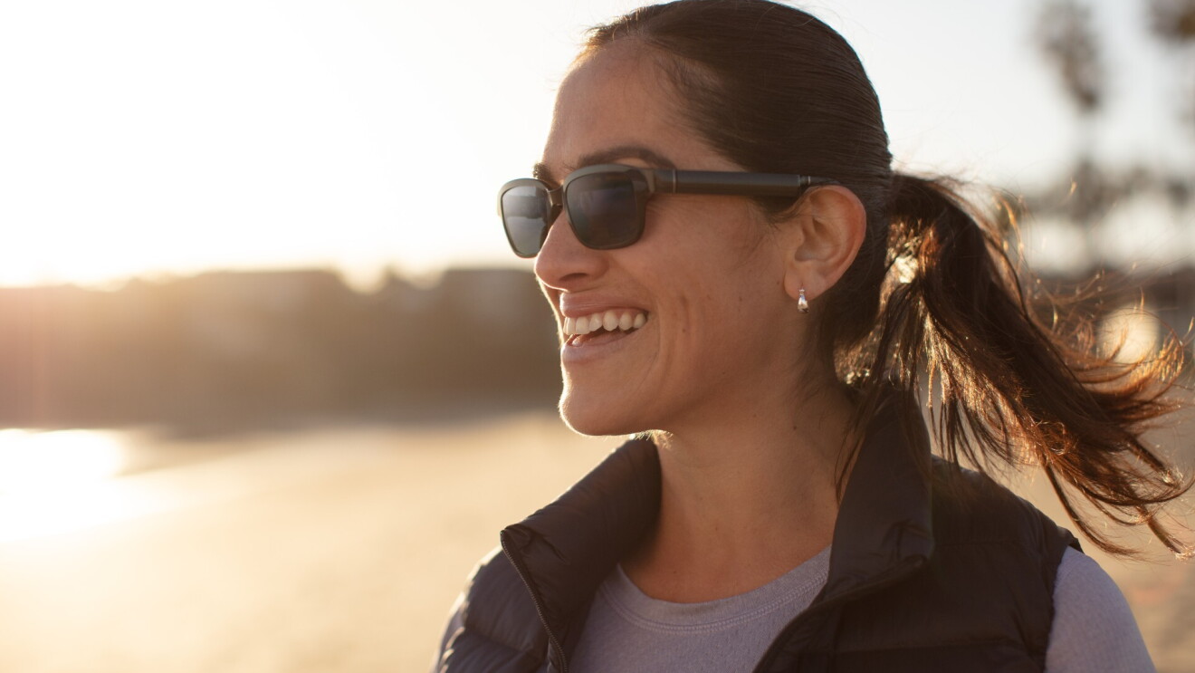 A woman wearing Echo Frames sunglasses while smiling watching the sunrise.