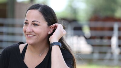 在这幅肖像中,一位黑发女子微笑着,看起来有点偏离镜头。她在外面,背景是一个马厩。