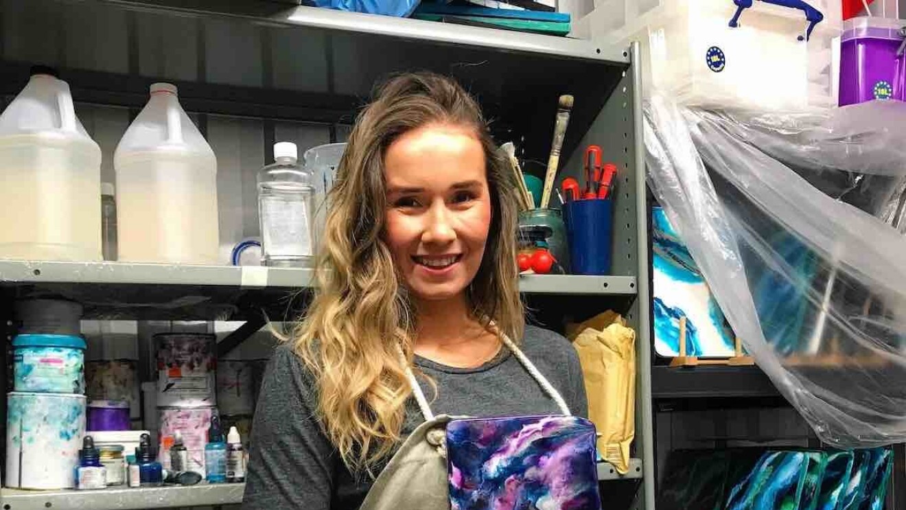 Kate Chesters holding one of her resin boards in her Liverpool-base studio, surrounding her are all of the utensils and products she uses to create her art.