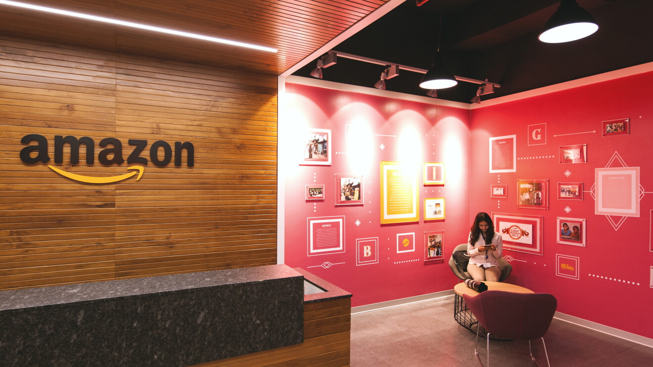 woman sitting in a chair reading from her phone. she is sitting inside an amazon office with red walls that contain artwork and graphics.