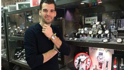Aurélien Cram se tient devant une vitrine remplie de montres et arbore une montre à son poignet