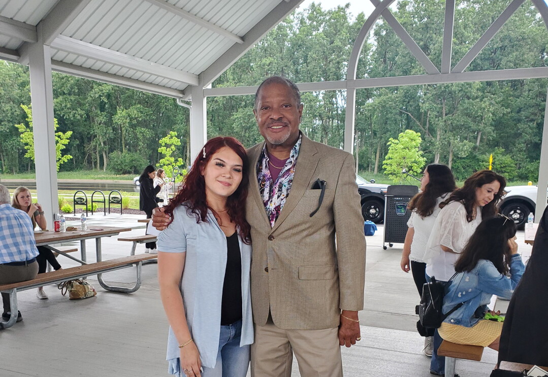 An image of a man and a woman standing together while smiling for a photo. They are at an event in a beautiful outdoor dining area.