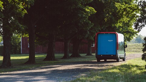 An electric delivery vehicle seen from behind, driving along a wooded road.