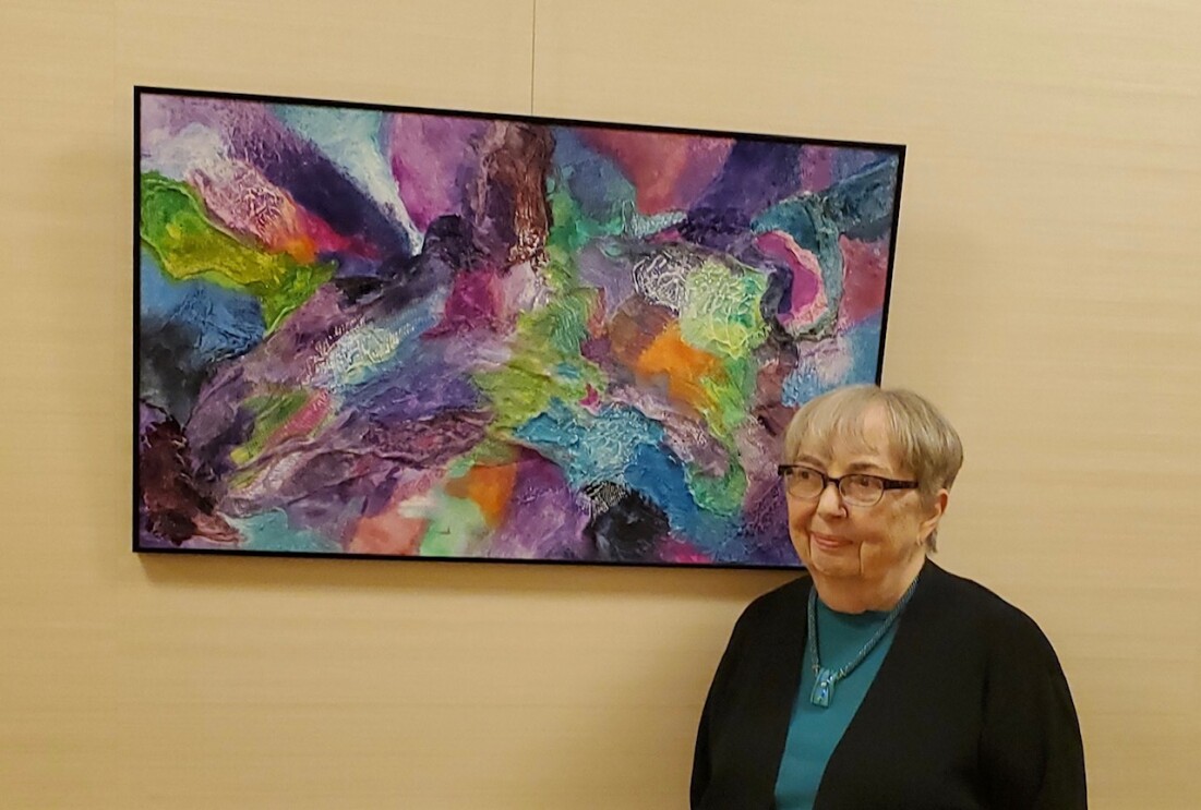 A woman stands in front of a colorful piece of art hanging on a wall.