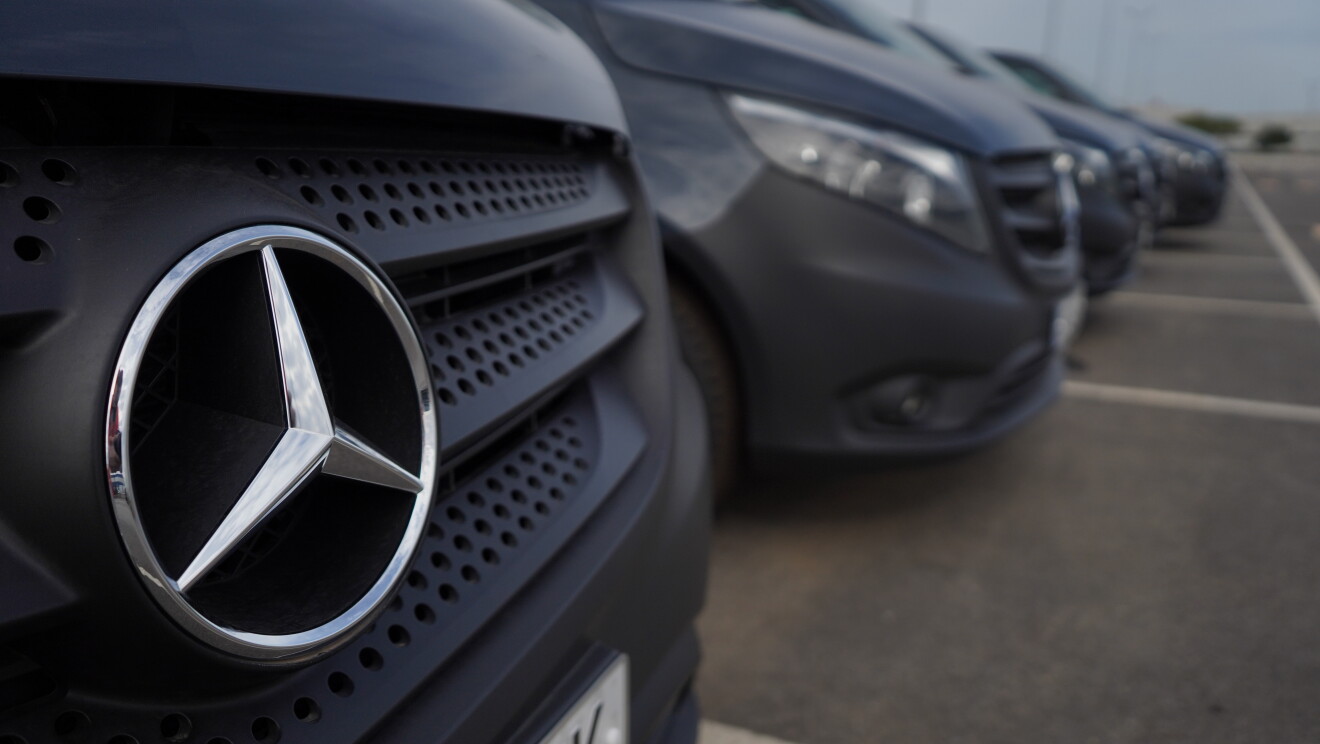 Una Mercedes Benz-Vans en un aparcamiento en primer plano. Detrás s even tres furgonetas más. En el primer plano se ve el logo de Mercedes-Benz. 