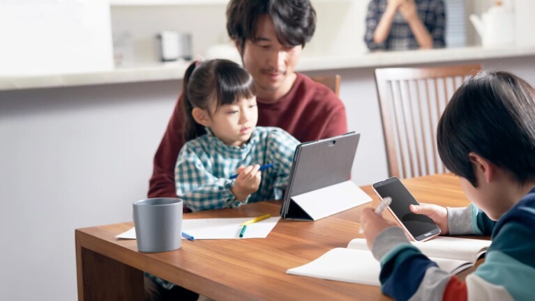 Family at dinner table using devices for schoolwork.