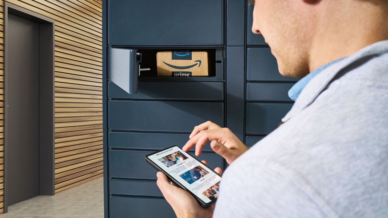 A man using his phone stands next to a wall of Amazon Lockers.