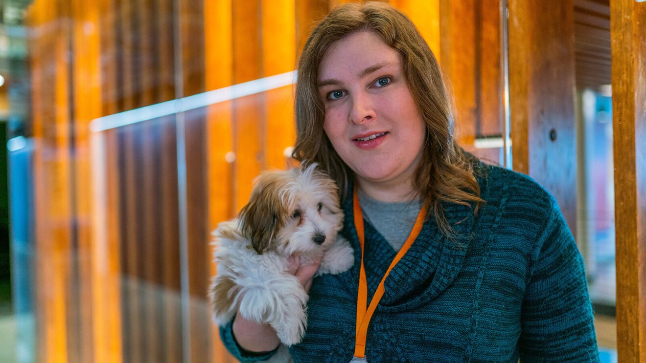 Ana Steele smiles for a photo with her small dog in front of a wood structure in Amazon's lobby.