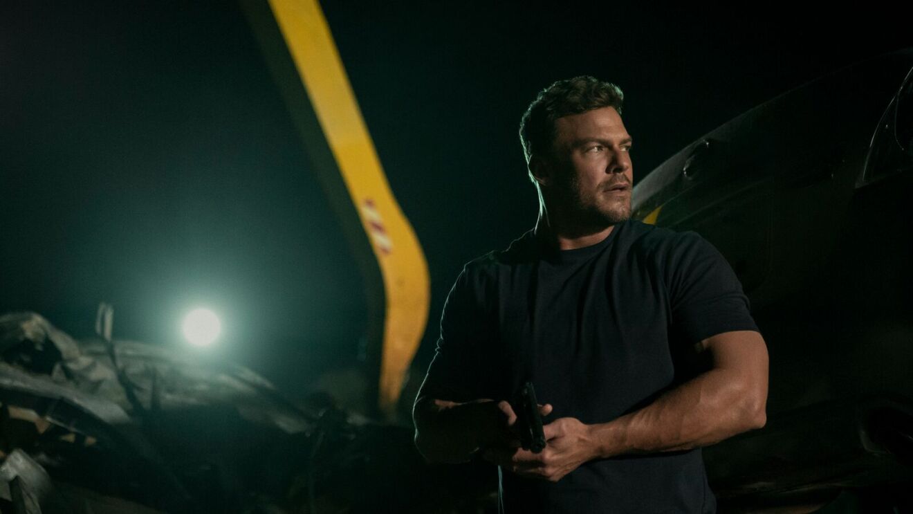 Alan Ritchson incarne Jack Reacher Alan Ritchson tient une arme dans une scène nocturne de Reacher