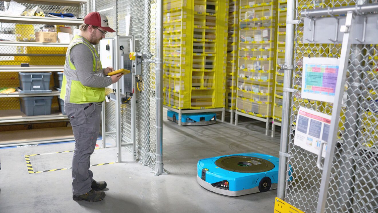 Amazon employee in safety vest managing automation system in storage facility