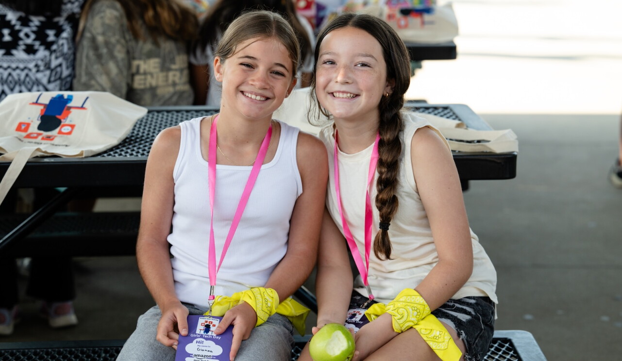 Two girls smile while seated on a bench during Amazon's Girls' Tech Day
