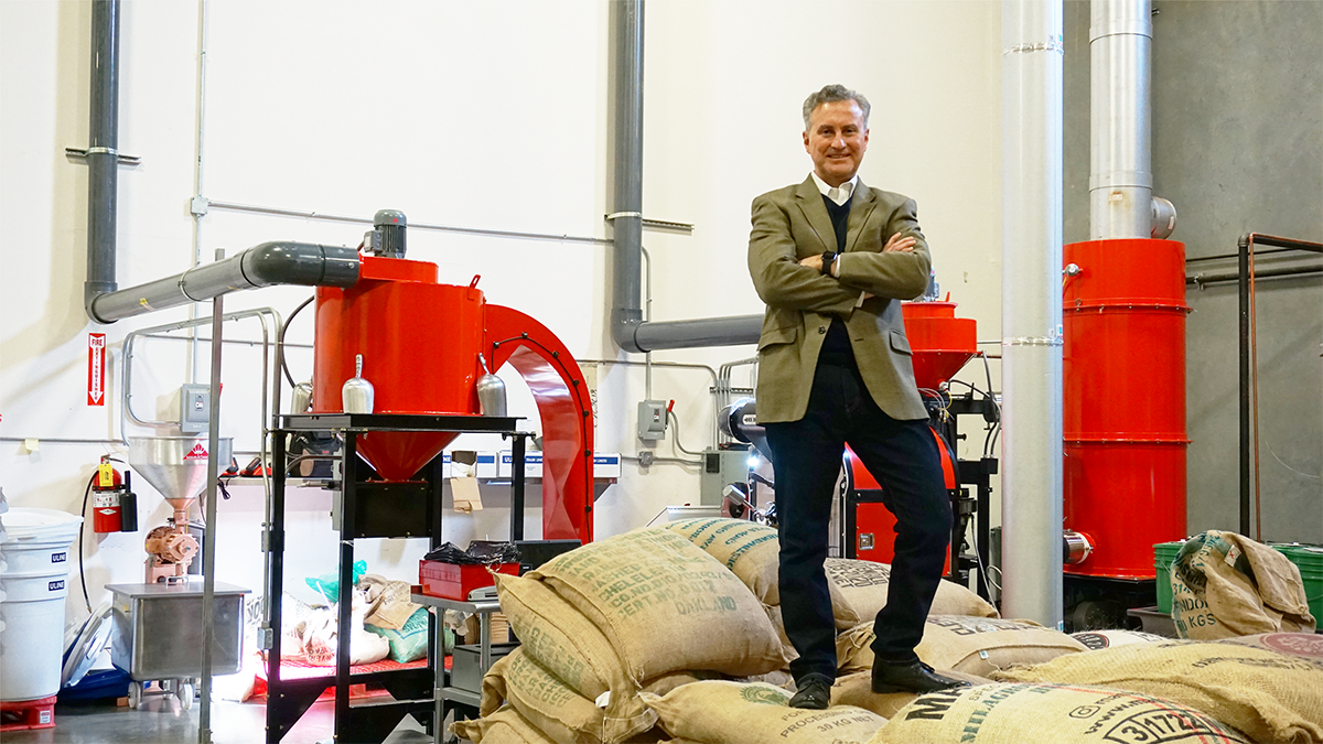 An image of a man standing on a pile of burlap sacks filled with a product in a factory.