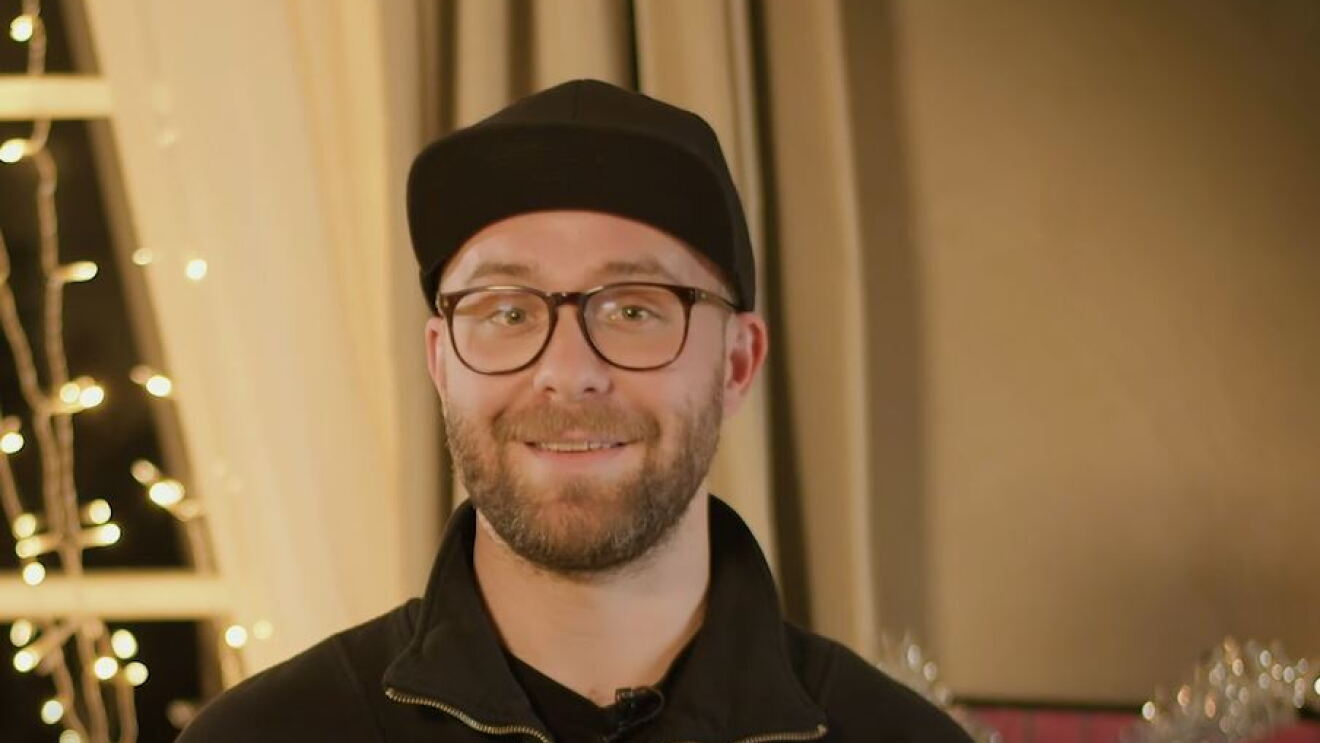 Mark Forster steht in einem weihnachtlich geschmückten Raum. Im Hintergrund sieht man die Deko und ein Kaminfeuer.