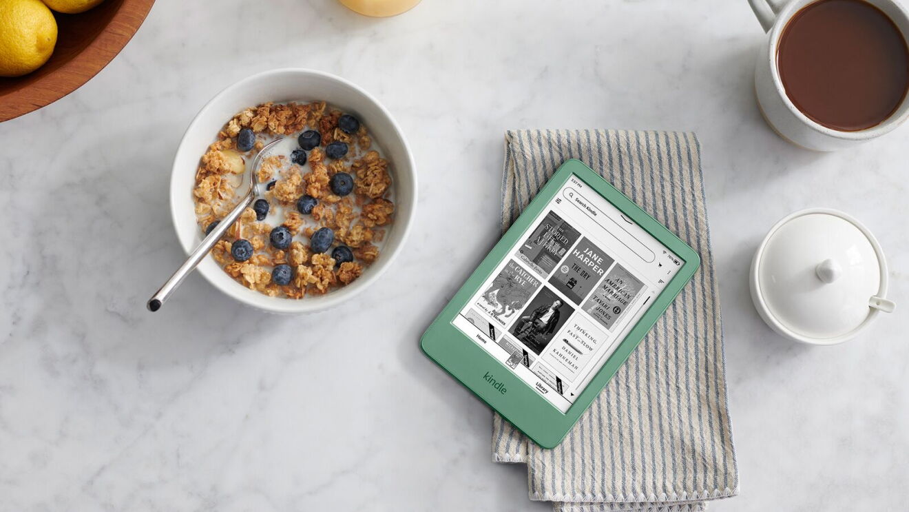 Breakfast table with granola bowl topped with blueberries, green Kindle e-reader, coffee mug, and fresh lemons