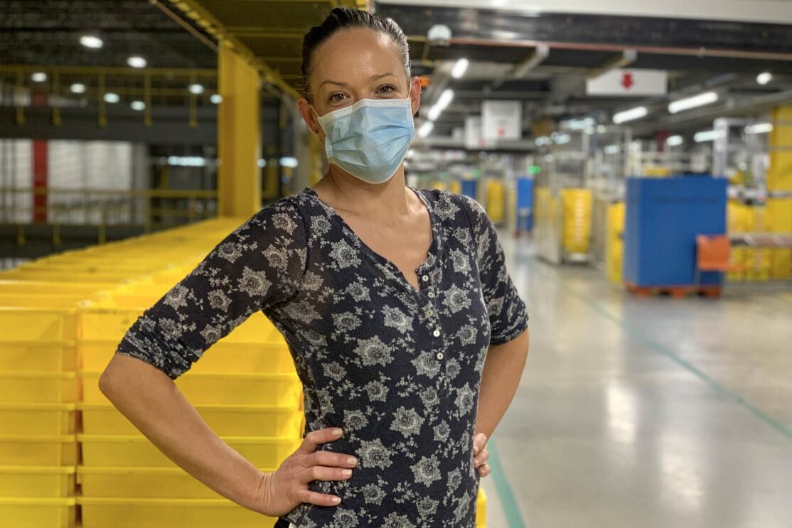 A woman wearing a mask stands in front of stacks of yellow plastic boxes. 