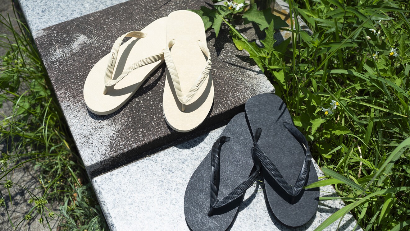 屋外のタイルの上に置かれた2足のビーチサンダル。クリーム色と黒