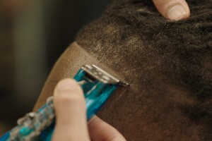 A close up image of a barber shaving the hairline of a client's forehead.