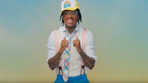 尼克大炮微笑的相机和他的两个大拇指,蓝色和黄色的影子背景。