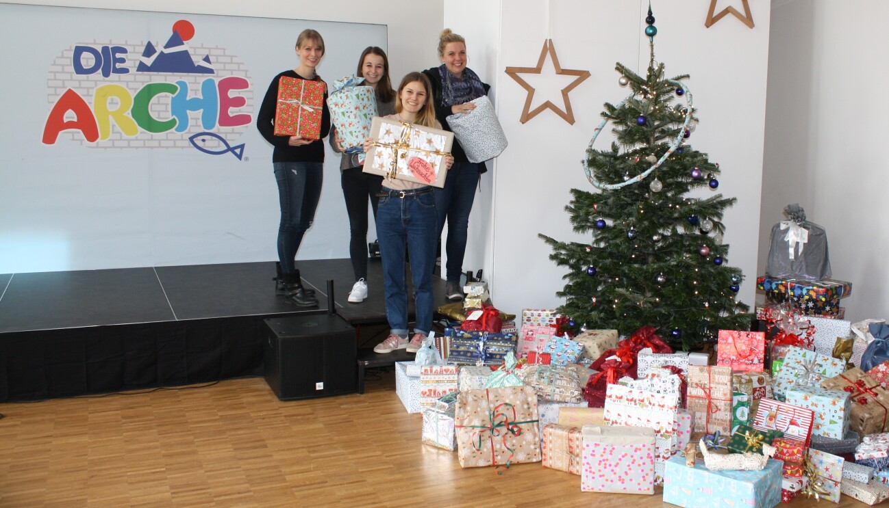 MItarbeiterinnen mit Geschnke stehen neben dem Weihnachtsbaum der Arche.