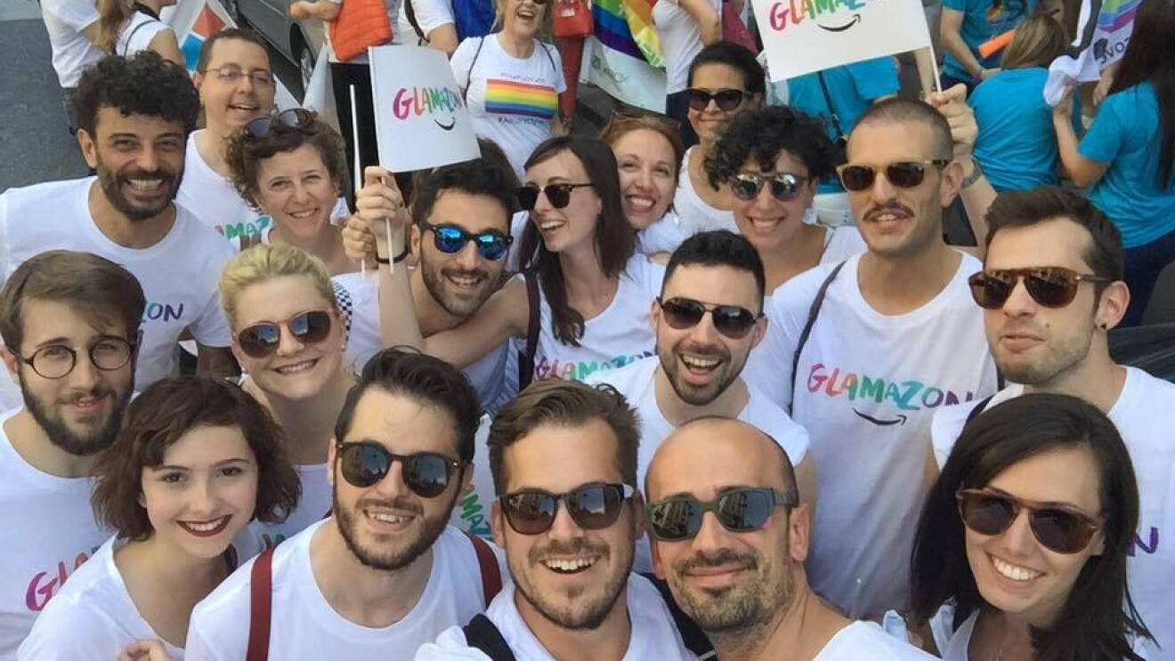 Gruppo di dipendenti Amazon in posa al Pride di Milano. Indossano una t-shirt con la scritta 'Glamazon' e molti di loro hanno gli occhiali da sole.