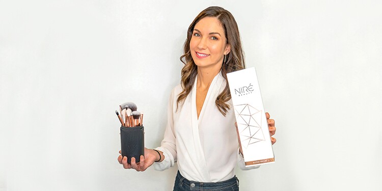 Owner of NIREBAUT Erin, holding up make-up brushes 