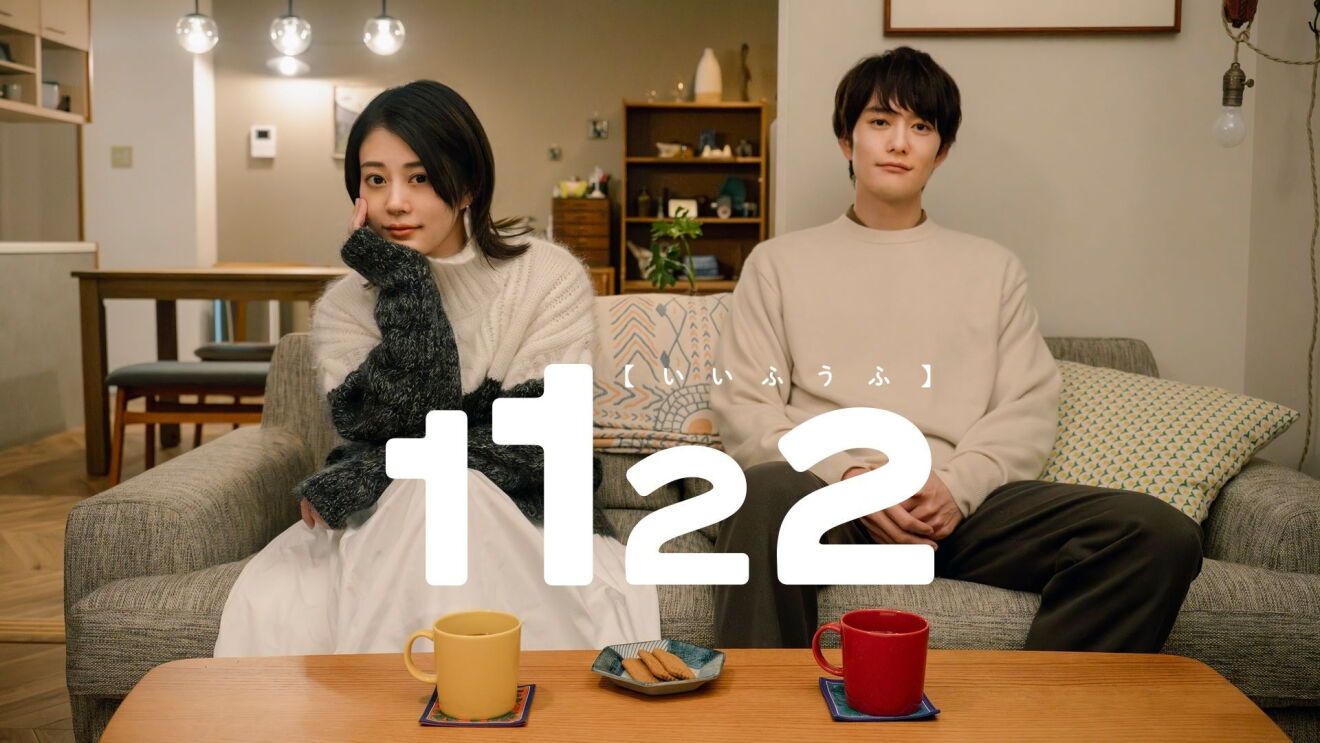 リビングのソファに座っている若い男女。その2人の前にあるテーブルには黄色と赤のマグカップとクッキーが載った小さなお皿がある