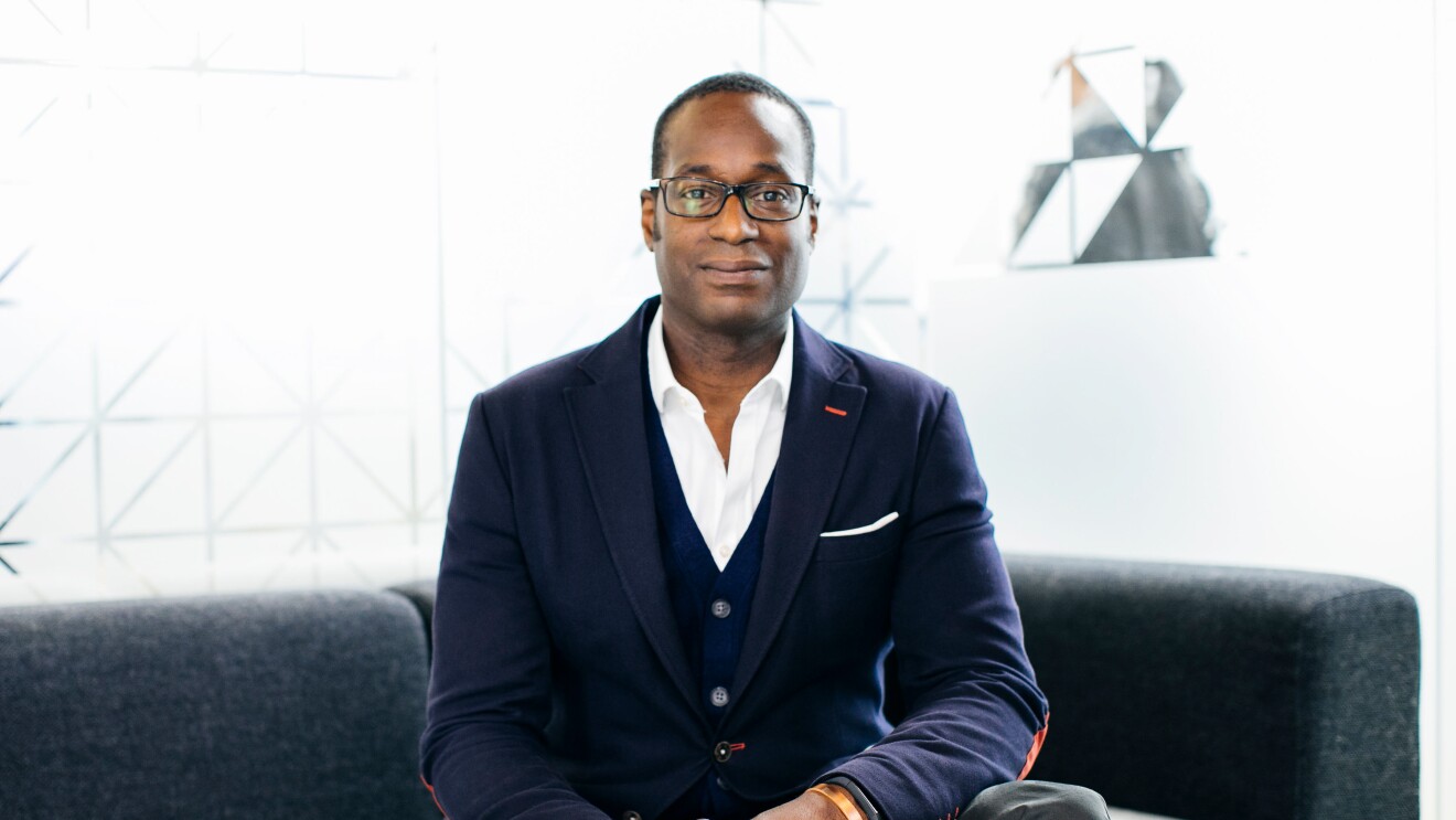 Oz Alashe dressed in a smart suit and sat on a sofa