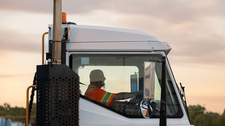 Truck driver in high-vis gear driving semi-truck at sunset