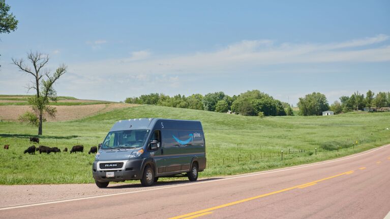 An Amazon delivery van is parked on the side of a road next to a pasture of cattle.